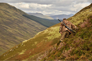 Hunter with scoped rifle trekking mountain highland terrain for long-range hunting