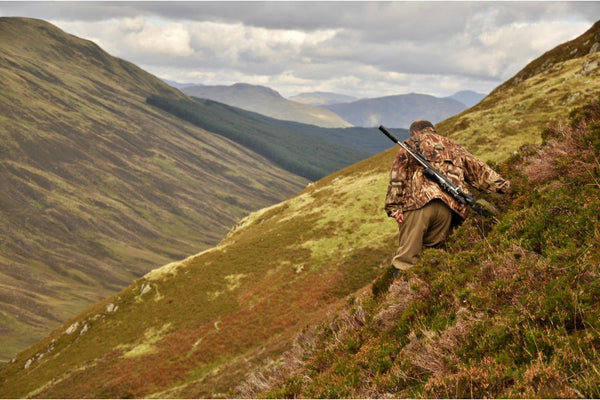 Hunter with scoped rifle trekking mountain highland terrain for long-range hunting