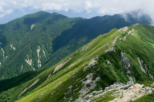 Green mountain ridge hiking trail, forest‑covered peaks, cloudy sky