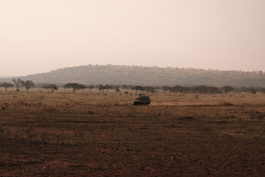 Safari vehicle on African savanna plain, hazy landscape.