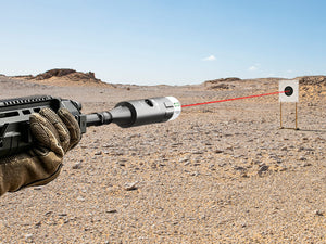 EZSHOOT laser bore sight projecting a red beam from a rifle toward a target in a desert landscape.
