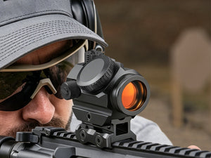 Close-up of a shooter aiming a rifle with a EZSHOOT red dot sight at an outdoor shooting range.